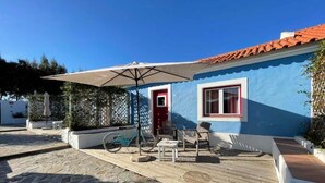 Una casa azul con puerta roja, terraza de madera y mobiliario exterior.