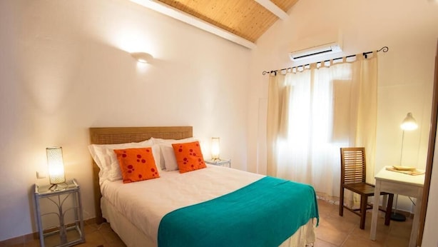 Een slaapkamer met een bed, nachtkastje, stoel, bureau en een raam met gordijnen.