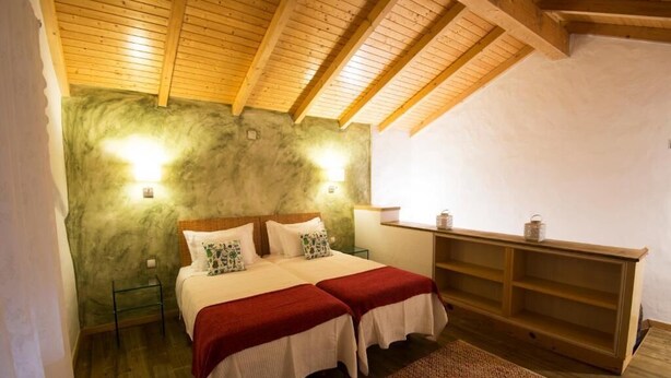 Un dormitorio con techo de madera, una cama con dos almohadas, una mesita de noche y un revistero.