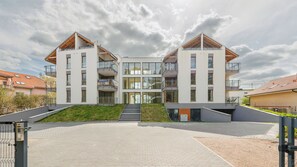 Ein modernes Mehrfamilienhaus mit Balkonen, einer zentralen Treppe und einem gepflasterten Eingangsbereich.