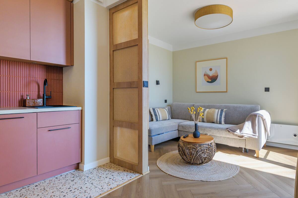 Un salon moderne avec un canapé, une table basse et un coin cuisine doté de meubles roses.