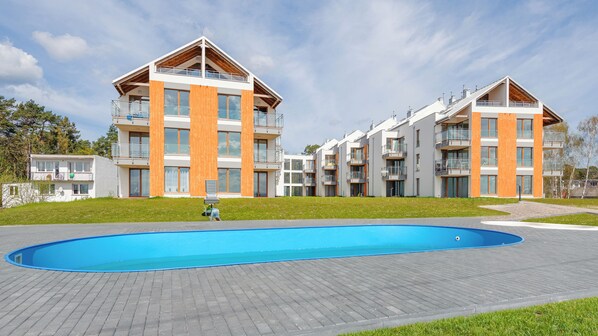 A modern apartment complex with a swimming pool, balconies, and a clear sky.