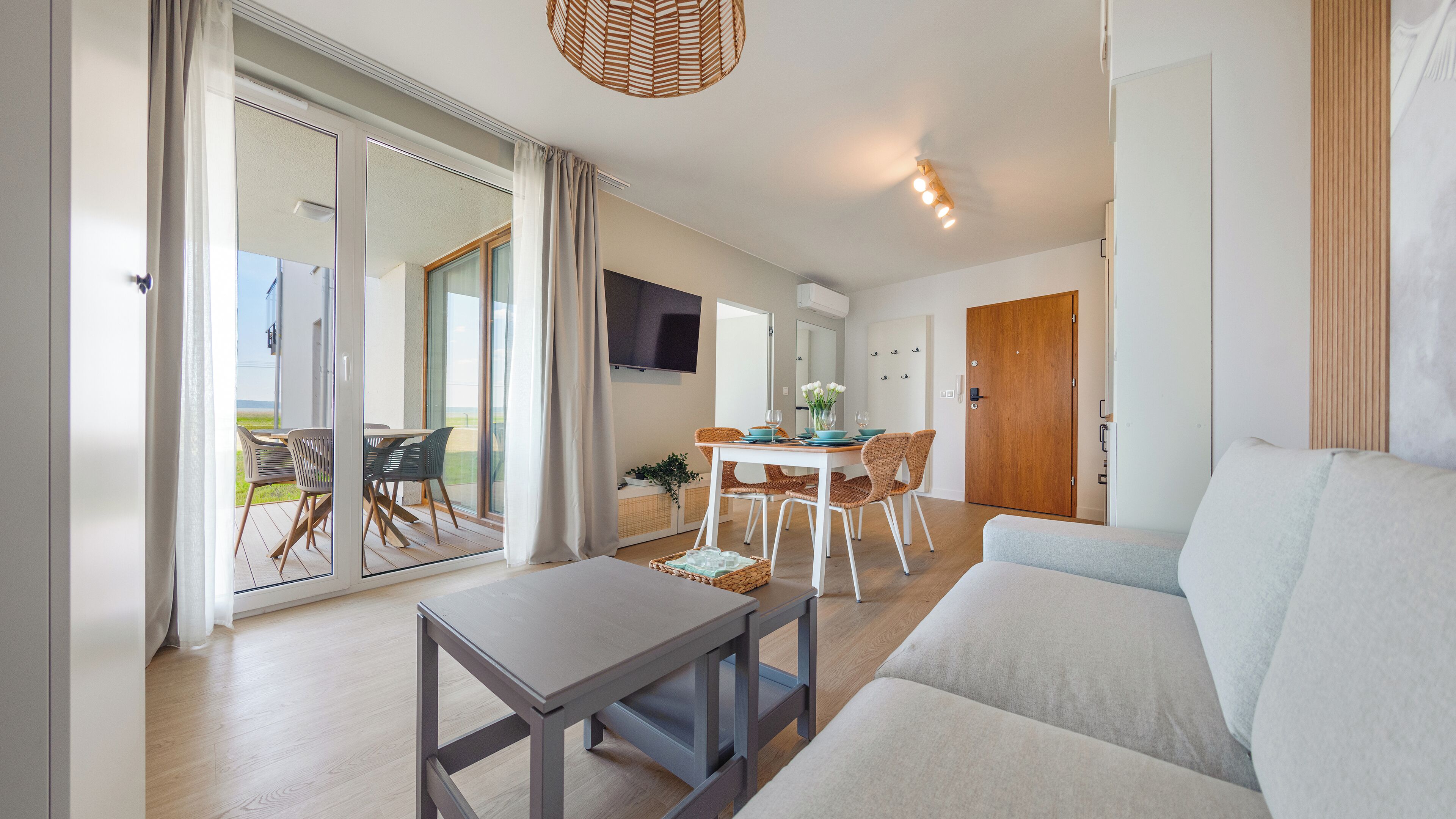 A modern living room with a sofa, a dining table with chairs, and a sliding glass door leading to a balcony.