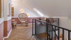 A spacious loft with a high ceiling, a rattan chair, a wooden table, and a staircase with a black railing.