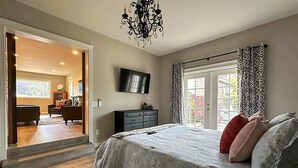 A bedroom with a large bed, a TV on the wall, and a chandelier.