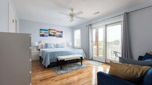 A bedroom with a bed, a bench, a desk, and a balcony with a view. - Whalehead Adventure With Ocean Views, Pool, Spa (Corolla)