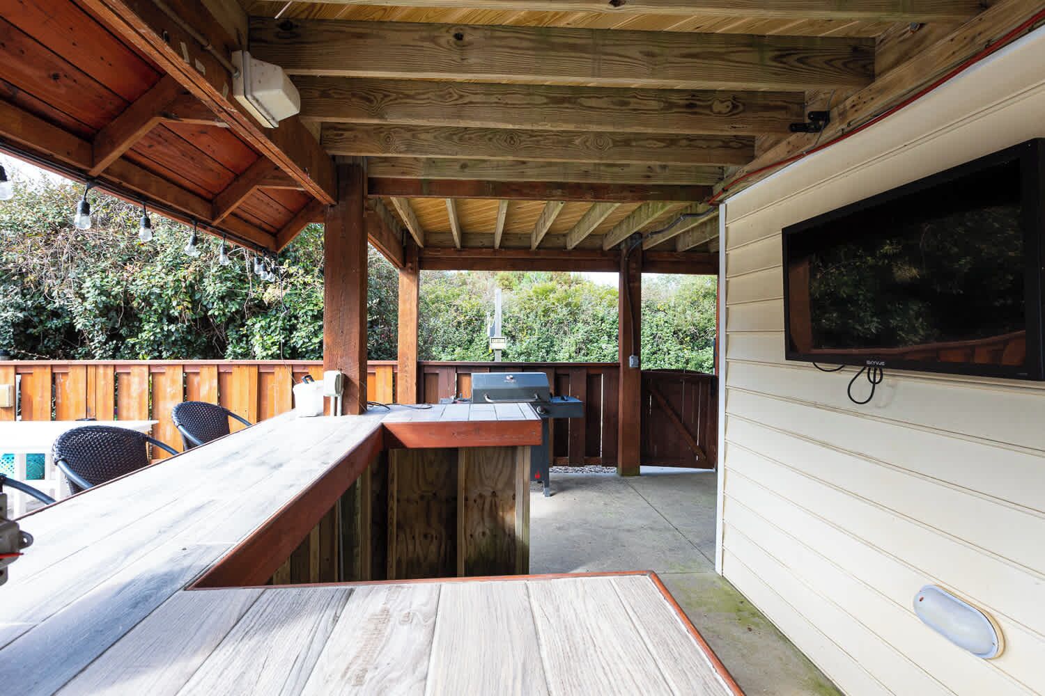Eine Terrasse im Freien mit Holzdeck, Grill und einem an der Wand befestigten Fernseher.