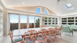 A spacious dining area with a large table and ornate chairs, large windows with a view, and a ceiling fan. - Oceanfront property with a private pool! (REHOBOTH BEACH)