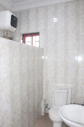 A bathroom with a toilet, sink, and a hand dryer mounted on the wall. - Pacific Paradise Suites (Uyo)