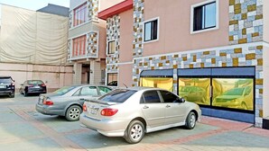 A building with a sign reading "Pacific Park Suites" and a covered parking area with several cars.