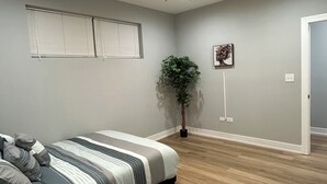 Un dormitorio con una cama, un ventilador de techo, una planta en maceta y una puerta que da a otra habitación.
