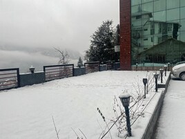 A snow-covered outdoor area with a metal fence, a building with glass windows, and a parked car.