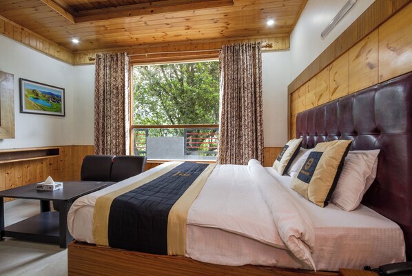 Une chambre d’hôtel avec un lit, un bureau et une vue sur les arbres par la fenêtre.