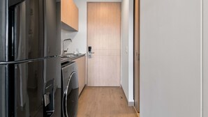 Une cuisine de taille réduite, équipée d’un réfrigérateur, d’un lave-linge et dotée d’une porte en bois.