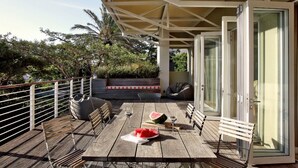 A wooden deck with a table set for two, a watermelon, and wine glasses. - The Library (Franschhoek)