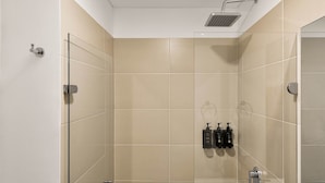 A modern shower with a glass door, beige tiles, and a handheld showerhead.