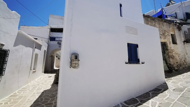 A white building with a small window and a door, set in a narrow street with stone pavement. - Authentic White House in Paros Lefkes (Paros)