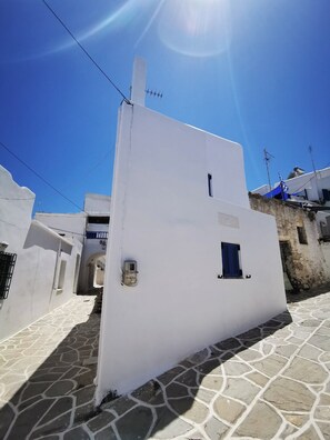 A white building with a small window and a door, set in a narrow street with stone pavement. - Authentic White House in Paros Lefkes (Paros)