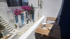 A balcony with a wooden table and chairs, a small white lantern, and a blue door with pink flowers. - Authentic White House in Paros Lefkes (Paros)