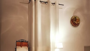 A bedroom with a wooden bed, a bedside table with a lamp, a chair, and a decorative plate on the wall. - Authentic White House in Paros Lefkes (Paros)