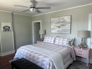 Una camera da letto con un letto, due comodini, una ventola a soffitto, un quadro e una porta.