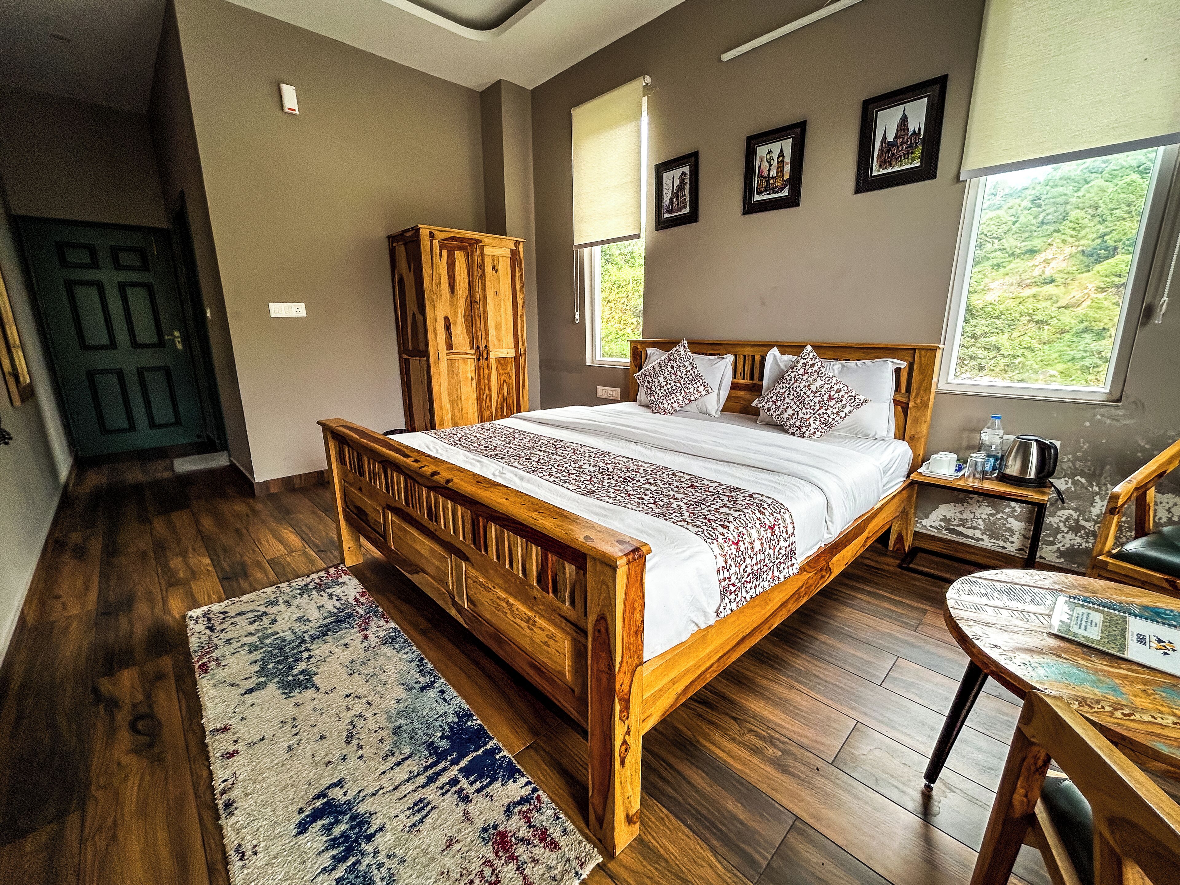 A bedroom with a wooden bed, a nightstand, a wooden wardrobe, and a view of greenery through the window.