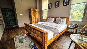 A bedroom with a wooden bed, a nightstand, a wooden wardrobe, and a view of greenery through the window.