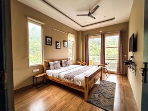 A spacious bedroom with a wooden bed, large windows, a ceiling fan, and a view of the outdoors. - Hotel Alchemy Bistro & Inn (Dharamshala)
