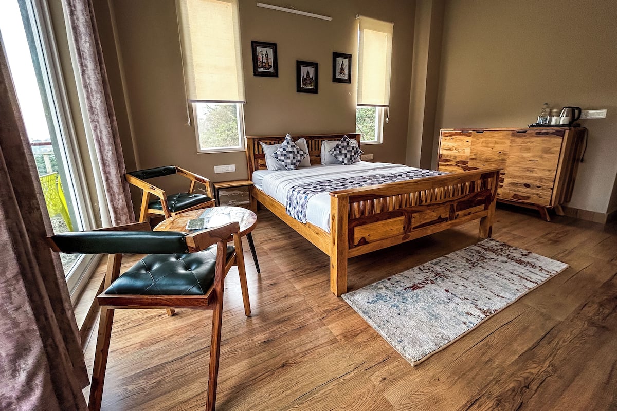 A bedroom with a wooden bed, a desk, two chairs, a dresser, and a window with curtains.