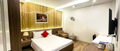 A modern hotel room with a large bed, a desk, a chair, a small table, and a wall-mounted TV.