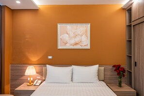 Une chambre d’hôtel avec un lit, une table de chevet, une lampe, un téléphone et un mur orné d’un tableau représentant des motifs floraux.
