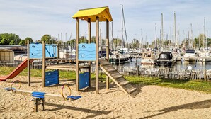 A playground with slides and swings, a sandy beach, and a marina with numerous boats. - 2 bedroom stunning ship in Naarden (Naarden)