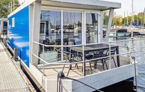 Une terrasse fermée par des baies vitrées, avec une table et des chaises, donnant sur une marina où sont amarrés des bateaux.