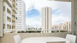 A balcony with a round table and four chairs, overlooking a cityscape with high-rise buildings.