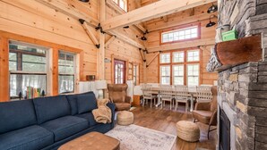 A cozy cabin interior with a wooden floor, a blue sofa, a dining table with chairs, and a stone fireplace.