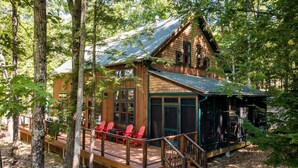 A cabin with a deck, red chairs, and a covered porch.