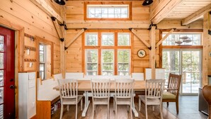 A wooden interior with a dining table and chairs, large windows, and a red door.