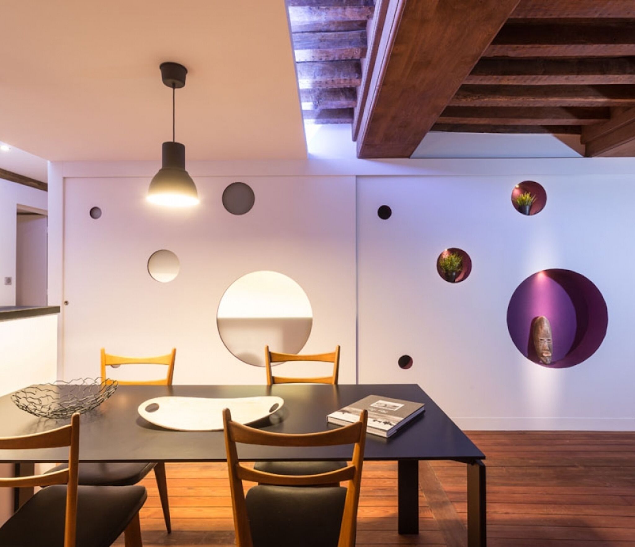 Un comedor moderno con una mesa oscura, sillas de madera y un aplique de techo.