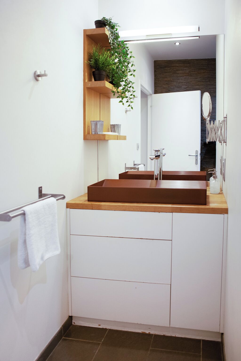 A modern bathroom with a wooden vanity, a large mirror, and a built-in shelf with plants.