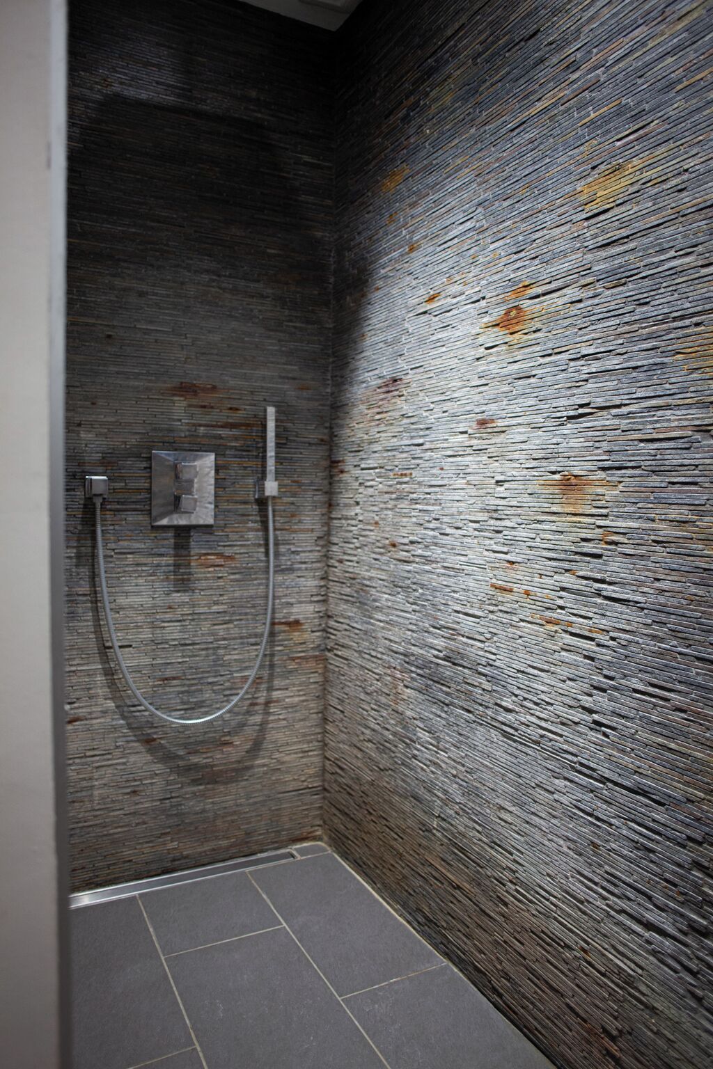 Une salle de bain avec un mur en pierre à texture, un espace douche et un sol carrelé.