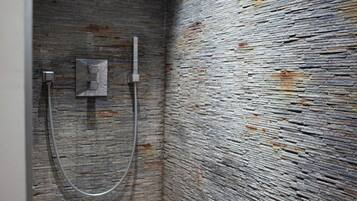 Une salle de bain avec un mur en pierre à texture, un espace douche et un sol carrelé.