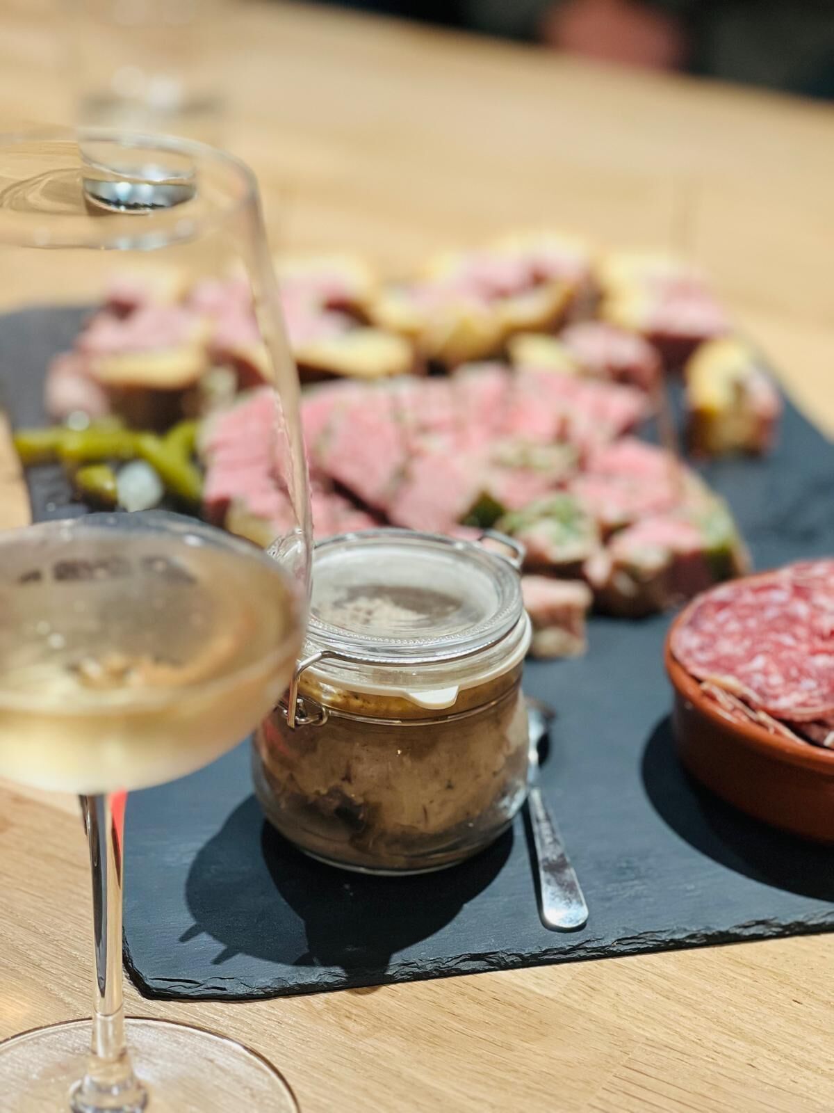 Ein Glas Weißwein, ein Klecks Sauce und geschnittenes Fleisch auf einer Schieferplatte.