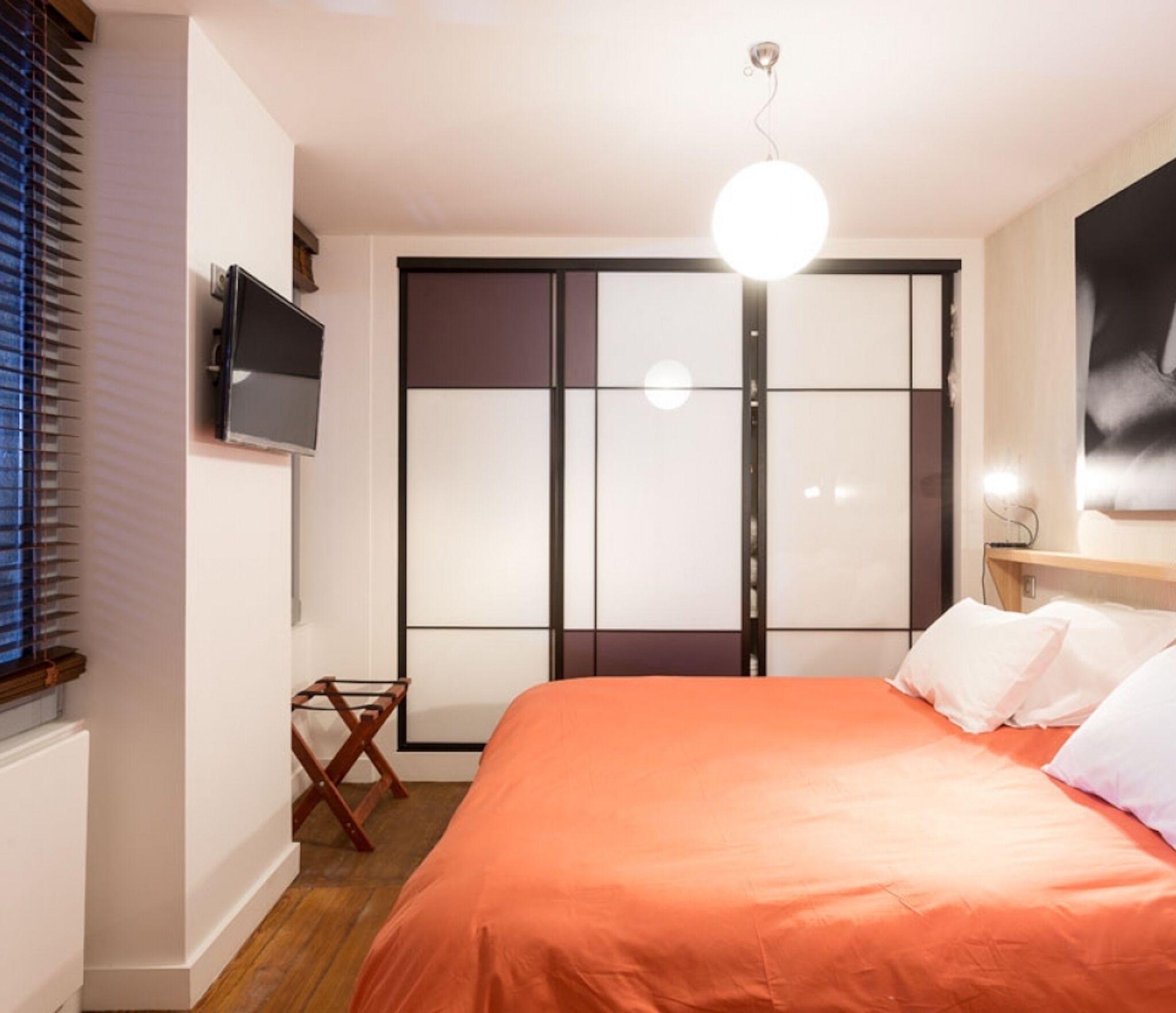 Een slaapkamer met een bed, een aan de muur bevestigde televisie en een schuifdeurkast.