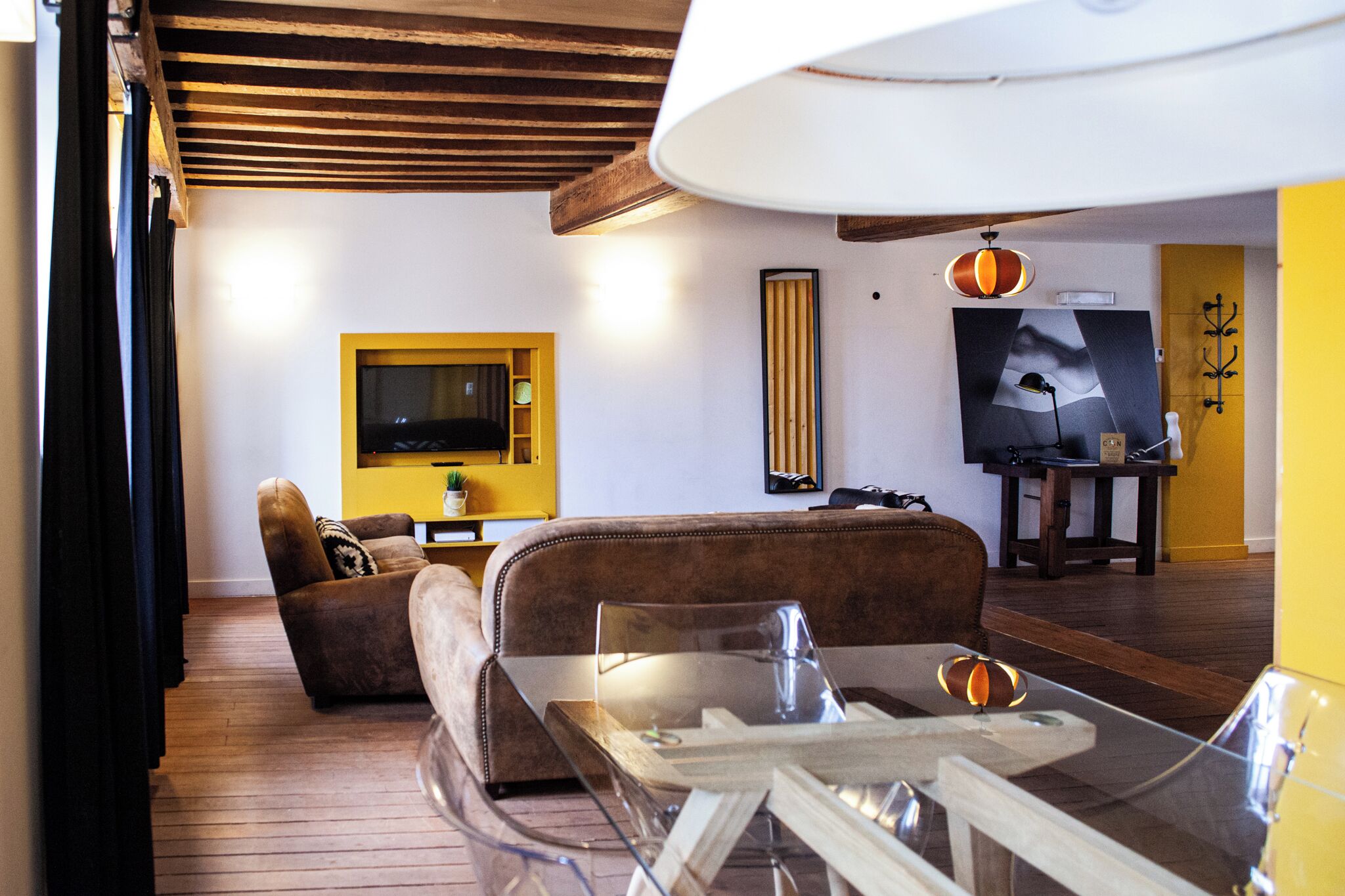 A living room with a sofa, a glass coffee table, a television mounted on the wall, and a yellow accent wall.