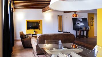 A living room with a sofa, a glass coffee table, a television mounted on the wall, and a yellow accent wall.