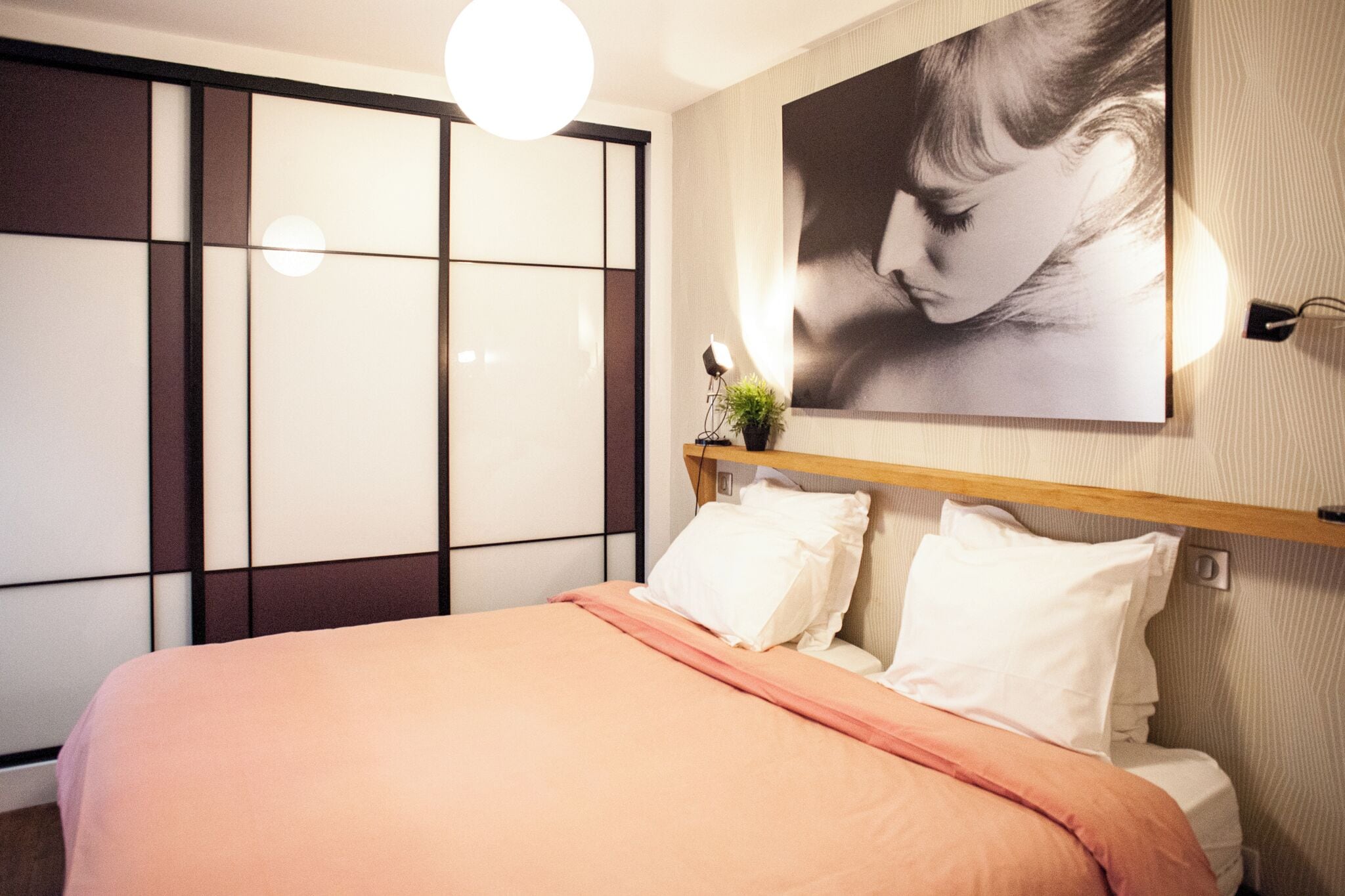 Une chambre à coucher avec un lit, une table de chevet avec une lampe, une étagère fixée au mur et un grand tableau encadré.