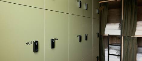 A row of green lockers with numbers 402 to 408, and a bunk bed with green curtains.