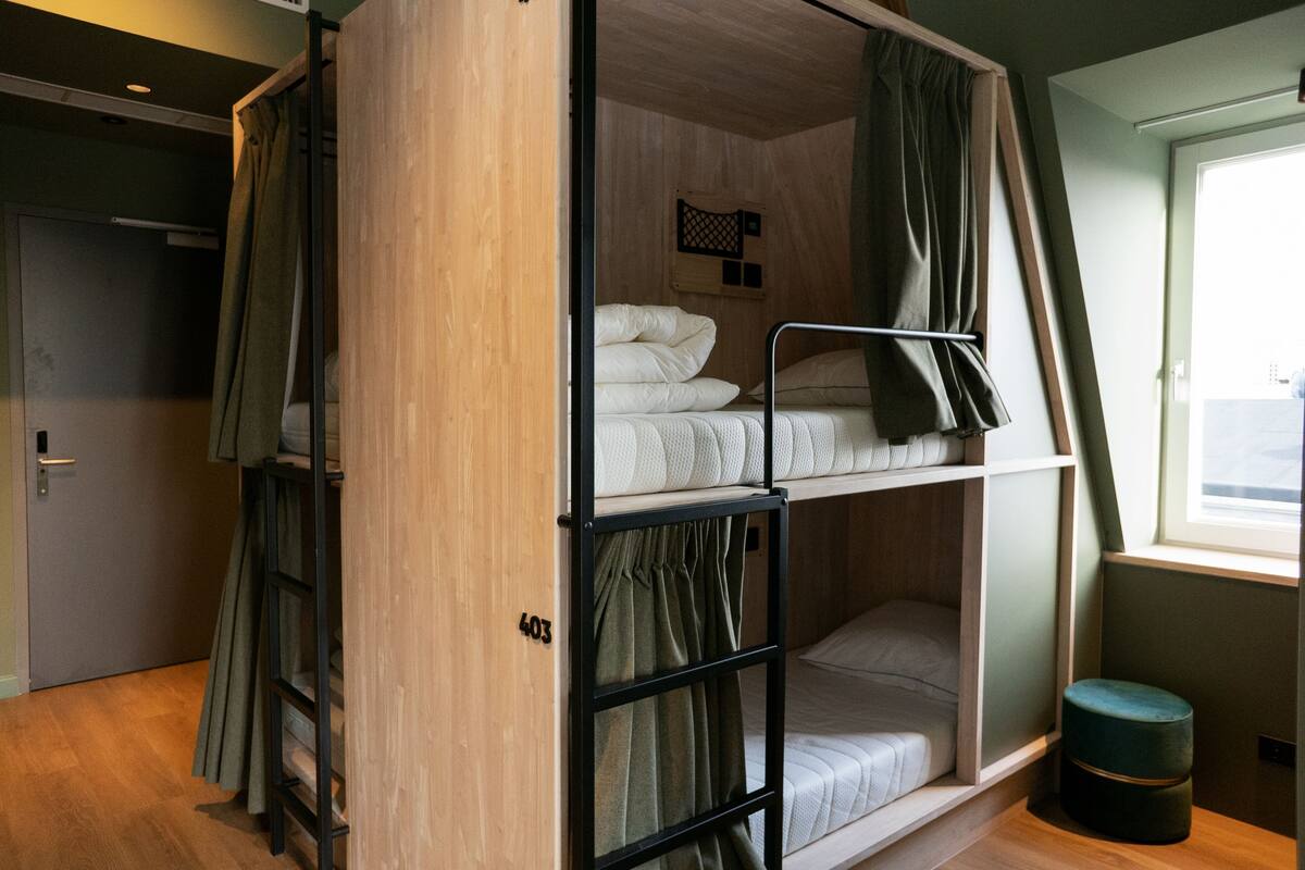 A bunk bed room with a wooden ladder, a small stool, and a window with curtains.