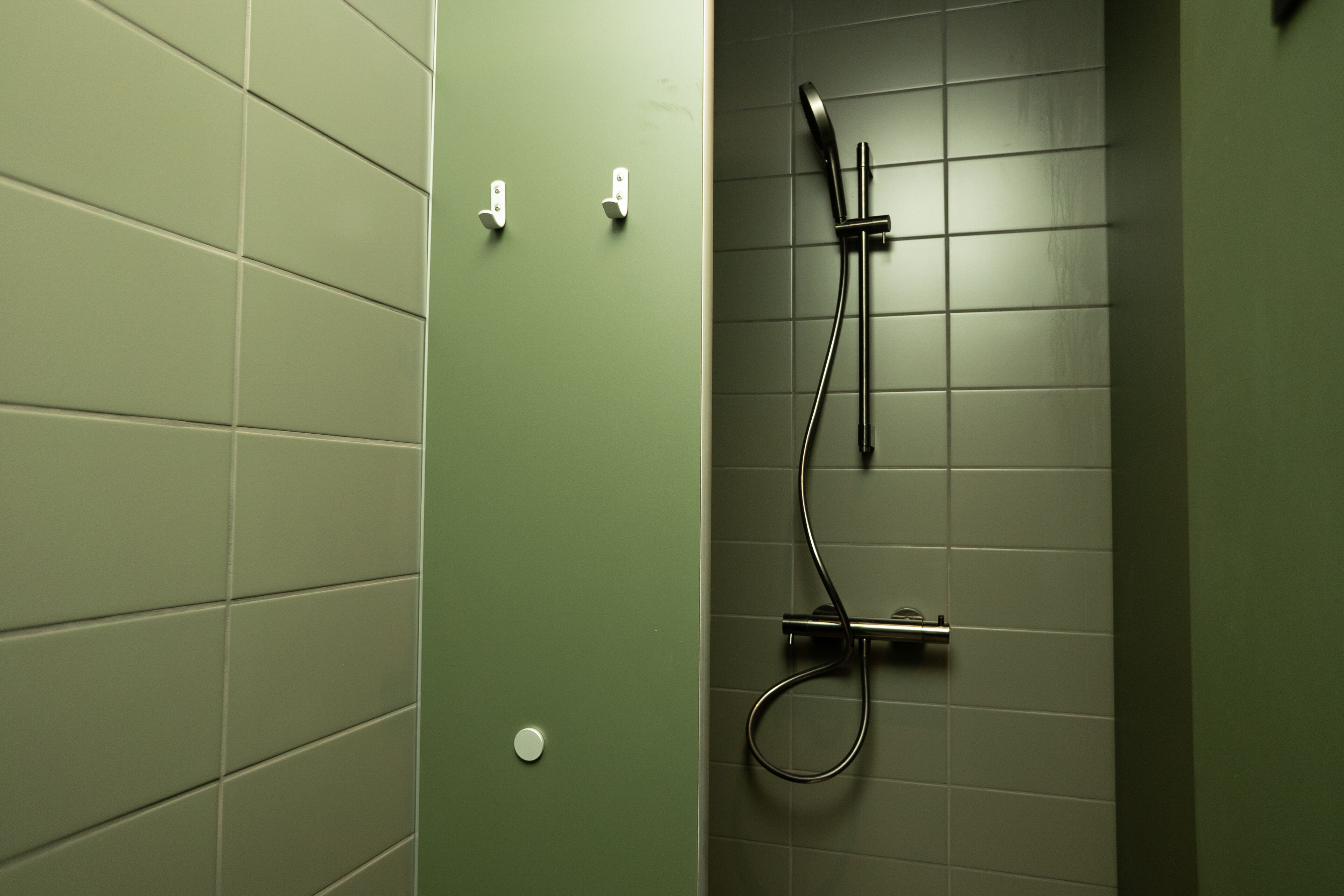 Un baño con paredes verdes, ducha con cabezal de ducha de mano y un perchero para toallas.