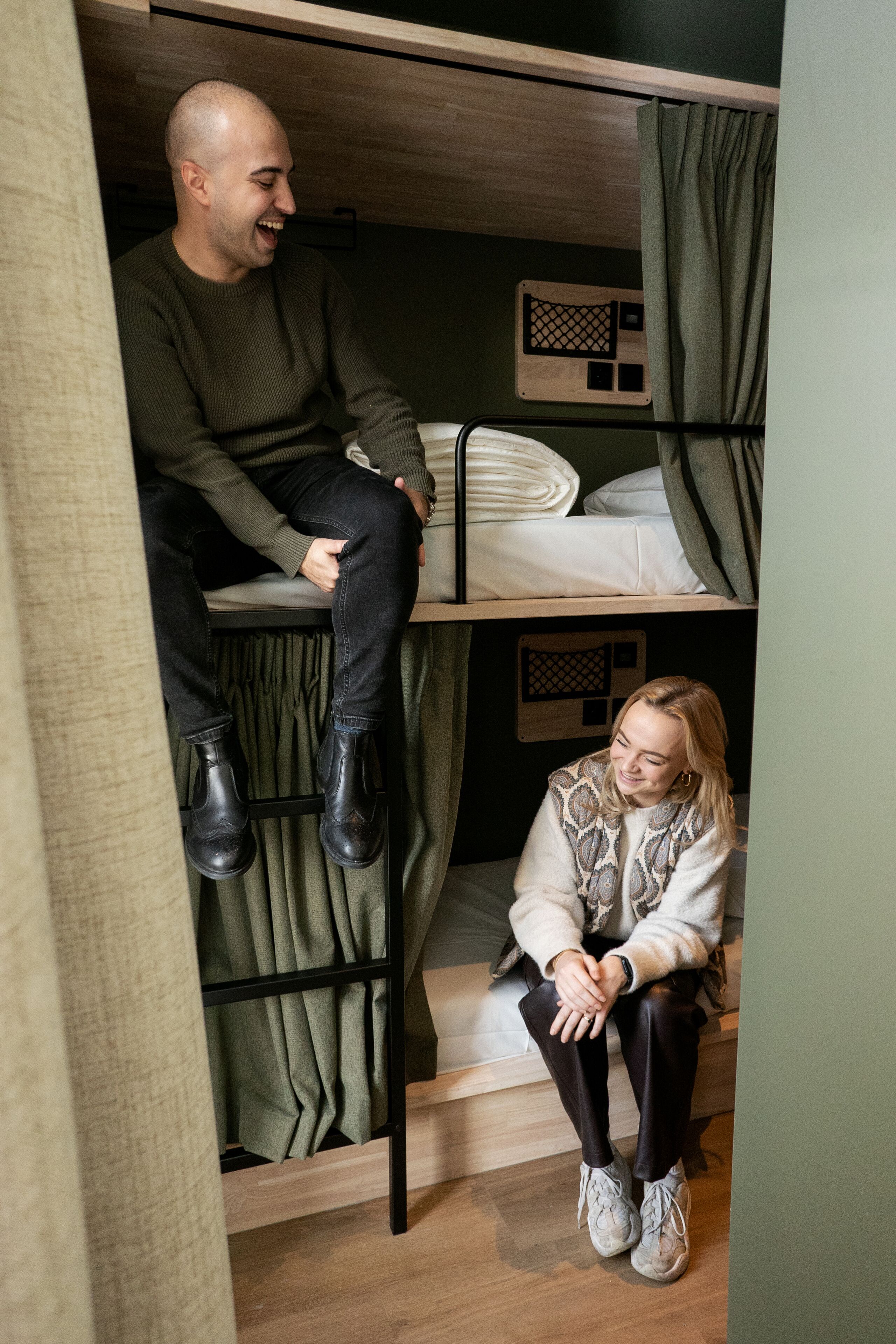 A bunk bed room with a wooden bunk bed, a lower bunk with a mattress and pillows, and a curtain.